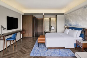 A hotel room with a bed, desk, chair, television, and a bathroom with a mirror and toilet. - Le Méridien Yichang Sanxia (Yichang)