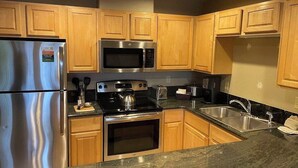 A kitchen with wooden cabinets, stainless steel appliances, a granite countertop, and a sink. - Grand Timber Lodge 3BR Resort Condo (Breckenridge)