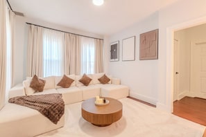 A modern living room with a sectional sofa, a round coffee table, and large windows with curtains.