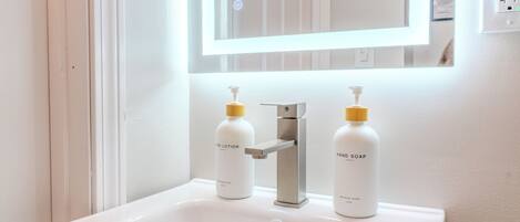 A bathroom with a white sink, two bottles of hand lotion, and a mirror above the sink.