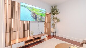A modern living room with a flat-screen TV, wooden panel wall, a plant, and a sofa. - NEW-Spacious 3BR-Office-Game Room-Laundry In Unit (Everett)