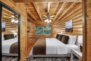 Ein Schlafzimmer in einer Blockhütte mit einem Bett, zwei Nachttischen, einem Deckenventilator, einem Fenster und einem Spiegel.