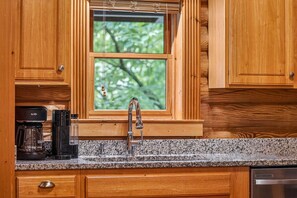 Eine Küche mit Holzausstattung, einer Arbeitsplatte aus Granit, einer Kaffeemaschine und einem Fenster mit Blick auf Bäume.