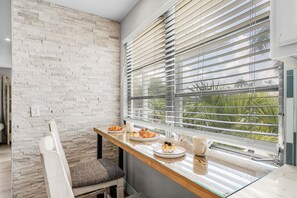 A breakfast setup with a table, chair, and window with blinds. - Private Beach Escape for Groups with Canal Views & Coastal Charm - Ocean Palms Retreat - Roelens (Fort Myers Beach)