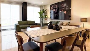 En moderne stue med spiseområde, en grøn sofa, et stort maleri og et gulv til loft-vindue.