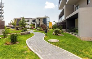 A modern building with a paved pathway, greenery, and a clear sky. - Cozy and Modern Apartment. (Juriquilla)