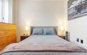 A bedroom with a bed, two bedside tables, a dresser, a wall-mounted heater, and a painting. - Cozy and Modern Apartment. (Juriquilla)