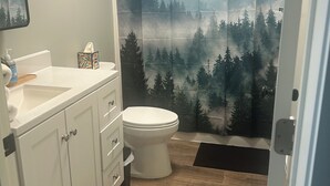 Une salle de bain avec des toilettes blanches, un lavabo surmonté d’un miroir et un tableau encadré accroché au mur.