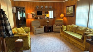 Ein gemütliches Wohnzimmer mit Holzwandverkleidung, einer Couch, Sesseln und einem kleinen Tisch.