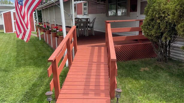 Eine rote Holzbrücke, die zu einem Haus mit Veranda, einer Flagge und einer Satellitenschüssel führt.