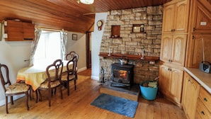 A cozy room with a stone fireplace, wooden cabinets, and a dining area with chairs and a table. - Gullane East (Killarney)