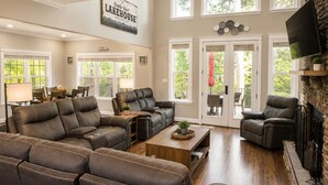 A spacious living room with leather sofas, a wooden coffee table, and a stone fireplace. - Lake Norman, Pool, Golf Simulator, Sauna, Hot tub, Pickleball/Basketball, EV Chg (Mooresville)