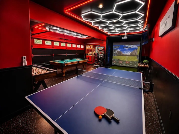 A room with a ping pong table, foosball table, and slot machines.