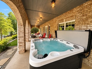 A hot tub in a covered outdoor area with brick walls and a view of a landscaped garden.