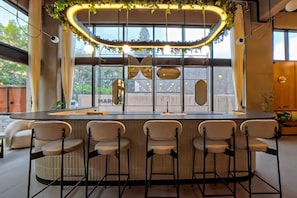 Zona de bar moderna con una lámpara curva, taburetes de bar y ventanas amplias.