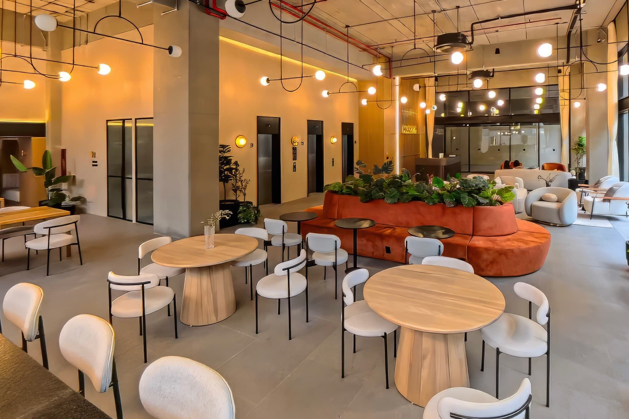 A modern interior with round tables and white chairs, a central orange sofa, and a large window.