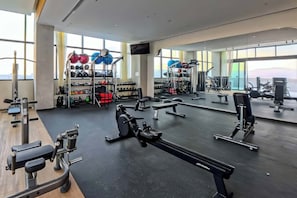 Een fitnessruimte met trainingsapparatuur, gewichtrekken en grote ramen.