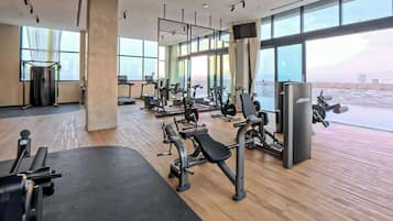 A modern gym with various exercise equipment, large windows, and a view of the sky.