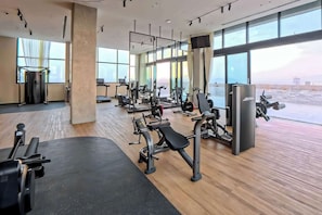 Un gimnasio moderno con diversos equipos de ejercicio, amplias ventanas y vista al cielo.