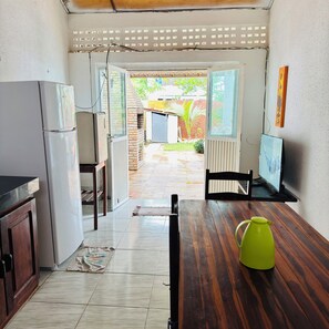 Eine Küche mit einem Kühlschrank, einem Esstisch mit einem grünen Krug und einer offenen Tür, die auf eine Terrasse führt.