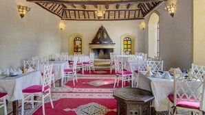 A dining area with white chairs, red carpets, and a central fireplace. - Riad Jnane Ines (Machraa El Ain)