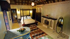 A traditional room with a bed, a mirror, a fireplace, and a small table with a flower arrangement. - Riad Jnane Ines (Machraa El Ain)