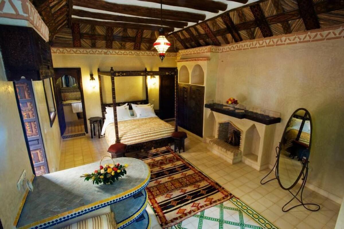 Une chambre traditionnelle avec un lit, un miroir, une cheminée et une petite table agrémentée d’un arrangement floral.