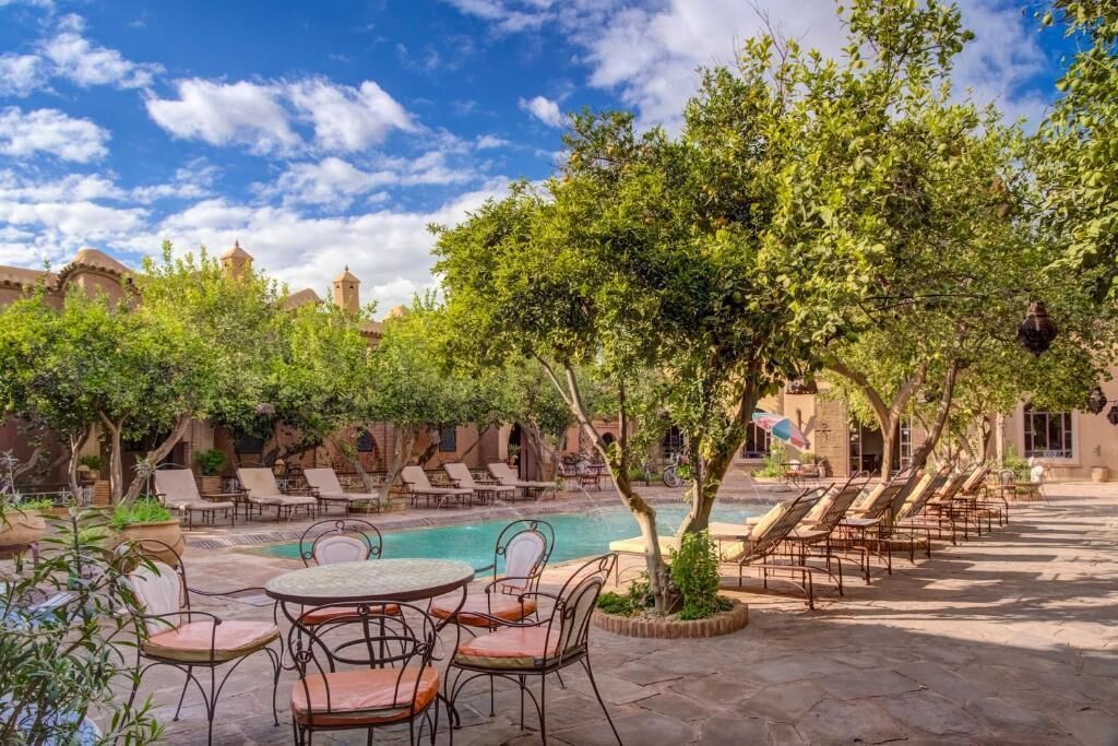 Zona de piscina con sillas de descanso, una mesa y un árbol.
