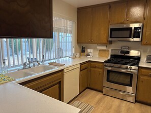 Una cocina con armarios de madera, electrodomésticos de acero inoxidable, una ventana con persianas y una encimera con cafetera.