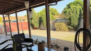Um pátio externo com móveis de vime, luminária pendente e vista para um estacionamento e área verde.
