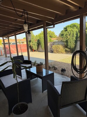 Un patio al aire libre con mobiliario de mimbre, una lámpara colgante y vistas a un estacionamiento y zonas verdes.