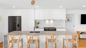 A modern kitchen with white cabinetry, a stainless steel refrigerator, a gas stove, and four wooden chairs. - Amos Court in Ocean Grove (Ocean Grove)