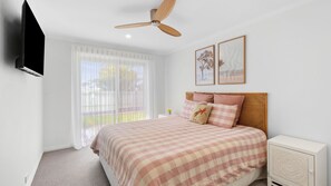 A bedroom with a bed, a ceiling fan, a TV, and a window with curtains. - Amos Court in Ocean Grove (Ocean Grove)
