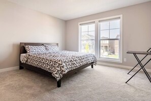 A bedroom with a bed, two windows, and a small table. - Green Bay Stay - 3BR, AC, Garage, Backyard, Self Check-in, Prof Cleaned (Calgary)