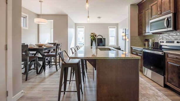 Una cocina moderna con una isla central, armarios de madera, electrodomésticos de acero inoxidable y un comedor con un ventanal grande.