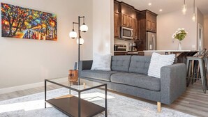 Una sala de estar moderna con un sofá gris, una mesa de centro de vidrio y un cuadro en la pared.