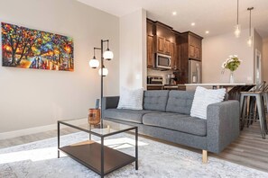 A modern living room with a gray sofa, a glass coffee table, and a painting on the wall. - Green Bay Stay - 3BR, AC, Garage, Backyard, Self Check-in, Prof Cleaned (Calgary)