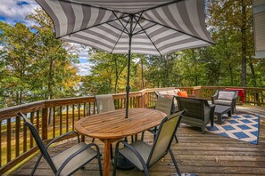 A wooden deck with a table and chairs, an umbrella, and a view of trees. - Beautiful Lakefront Home With Fireplace, Deck, Central AC, & Washer/dryer (Mineral)