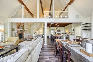 A spacious living area with a fireplace, a dining table set with a centerpiece, and a kitchen in the background. - Beautiful Lakefront Home With Fireplace, Deck, Central AC, & Washer/dryer (Mineral)
