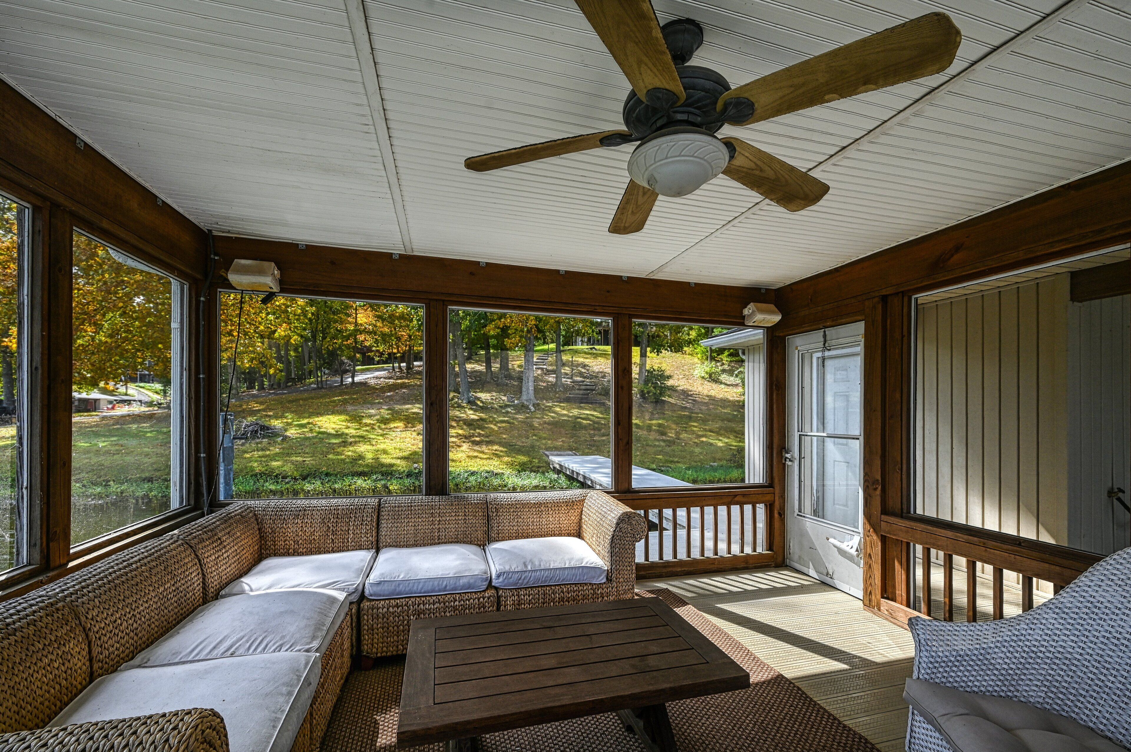 A covered porch with a ceiling fan, wicker furniture, and a view of a yard.