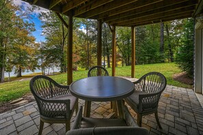 An outdoor patio with a round table and four chairs, surrounded by a wooden pergola, overlooking a lake and wooded area. - Beautiful Lakefront Home With Fireplace, Deck, Central AC, & Washer/dryer (Mineral)