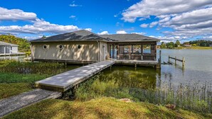 Uma casa à beira do lago com um cais, varanda coberta e um pequeno barco.