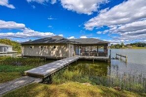 A lakeside house with a dock, a covered porch, and a small boat. - Beautiful Lakefront Home With Fireplace, Deck, Central AC, & Washer/dryer (Mineral)