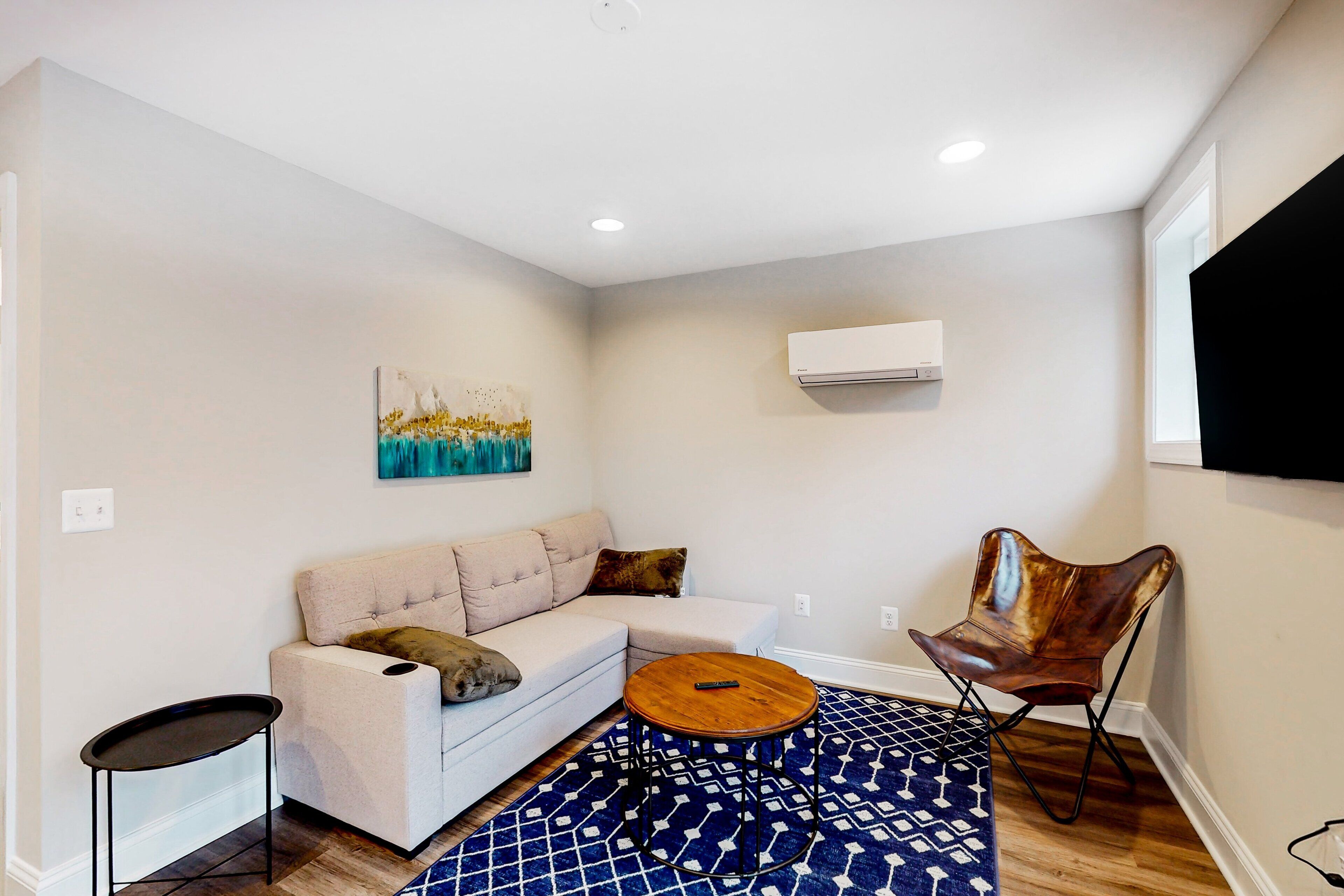 A living room with a sofa, a coffee table, a patterned rug, and a wall-mounted TV.