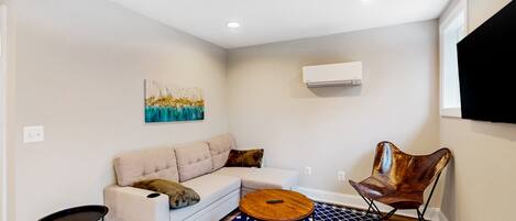 A living room with a sofa, a coffee table, a patterned rug, and a wall-mounted TV.