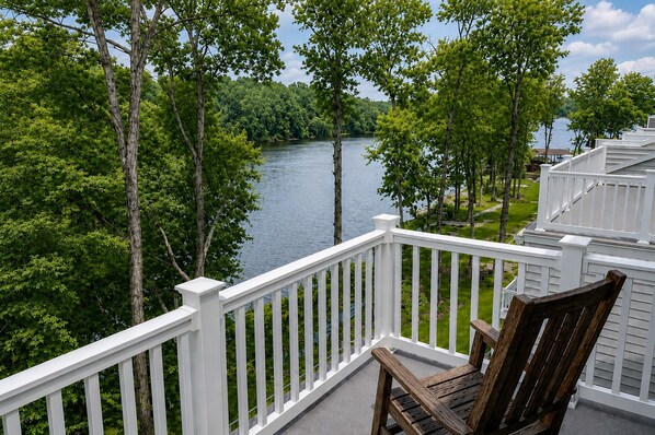 A balcony with a view of a river and forest, a wooden chair, and a white railing. - Charming Lakefront Retreat With Game Room and Covered Dock Access (Mineral)