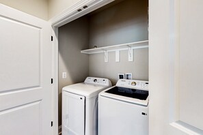 A laundry room with two white washers and dryers, a white shelf above, and a white door. - Charming Lakefront Retreat With Game Room and Covered Dock Access (Mineral)