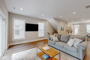 A living room with a gray sofa, a coffee table, a TV mounted on the wall, and a staircase leading to an upper level. - Charming Lakefront Retreat With Game Room and Covered Dock Access (Mineral)