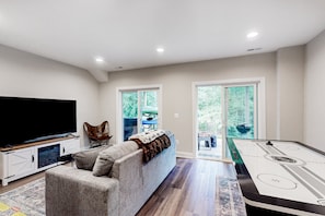 A living room with a flat-screen TV, a sofa, a pool table, and a sliding glass door leading to an outdoor area. - Charming Lakefront Retreat With Game Room and Covered Dock Access (Mineral)