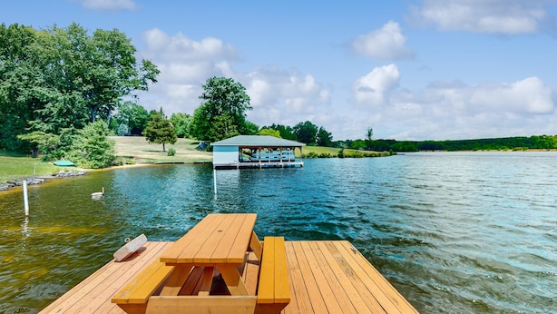 A wooden dock with a picnic table, a small boat, and a covered area on the water. - Charming Getaway With a Fireplace, Large Deck, Paddle Boards & Porch Swing (Mineral)
